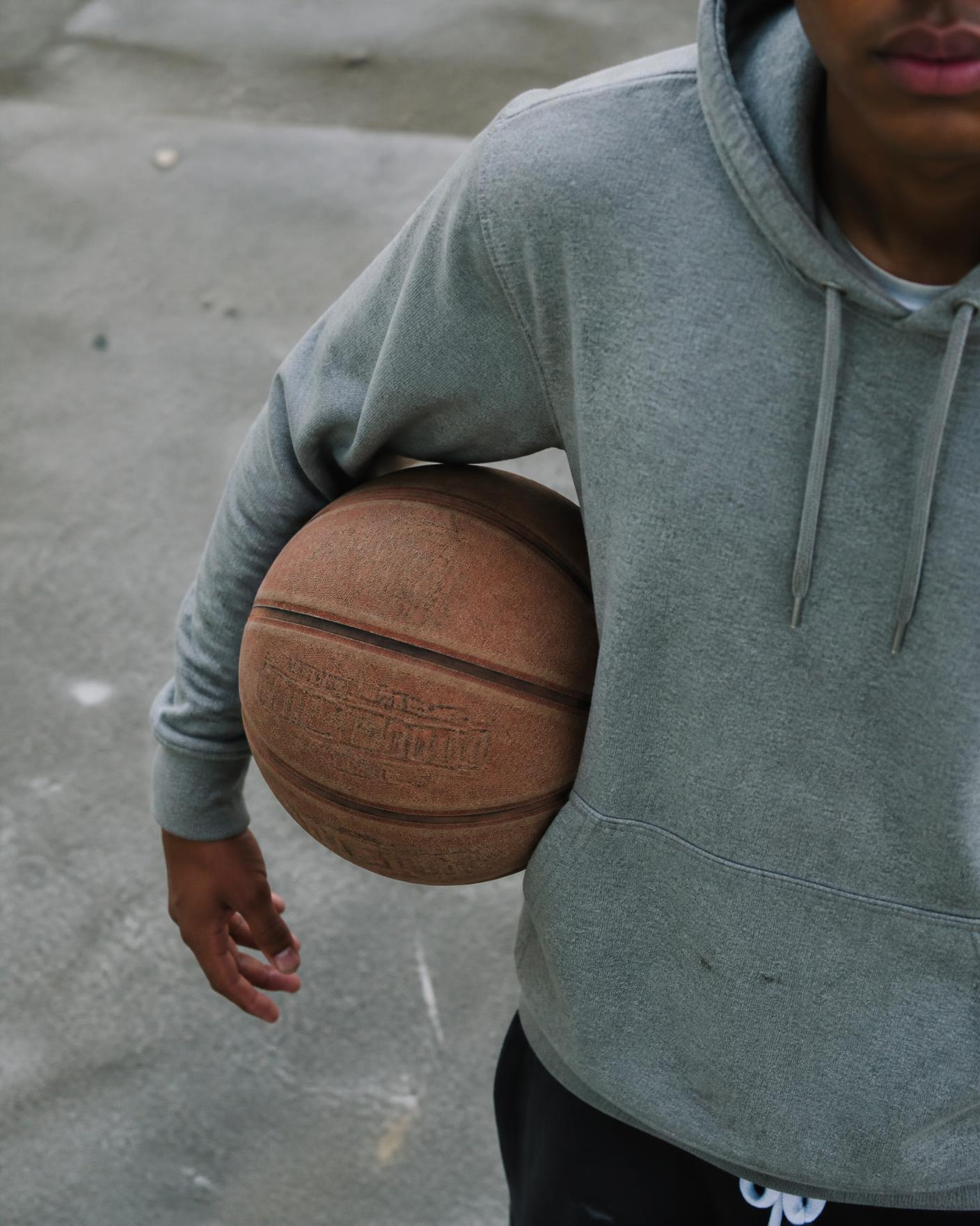 A worn leather basketball tucked under a grey hoodie sleeve