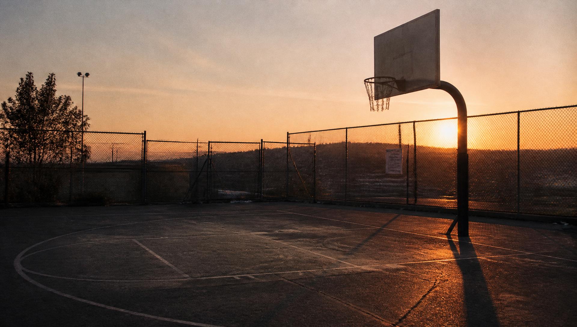Empty outdoor basketball court at sunset, warm light across the blacktop