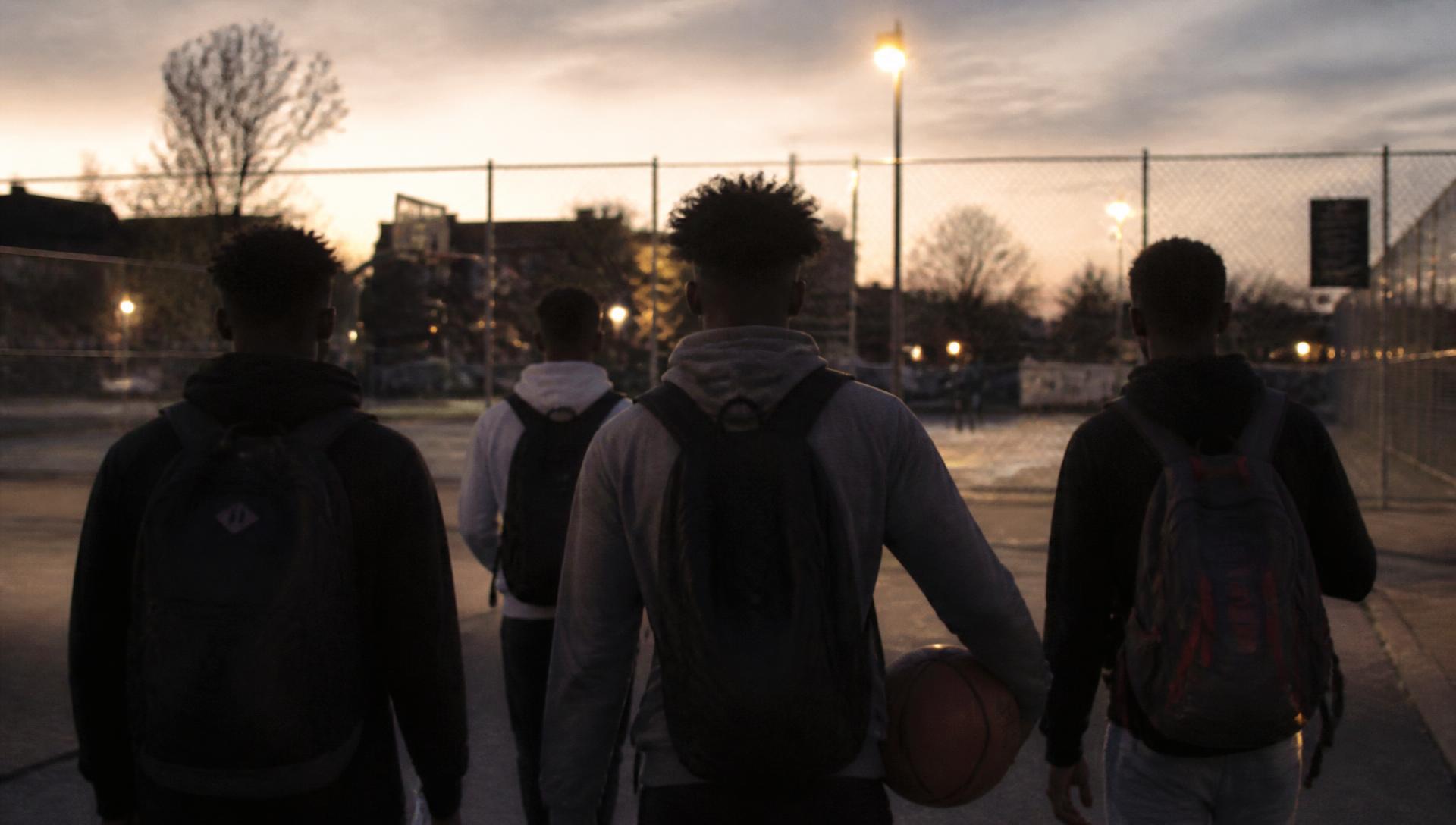 Friends walking toward a neighbourhood street court as the streetlights come on